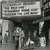 Black and white photograph showing figures in what appears to be an interior or storefront setting; image quality is grainy with low contrast.