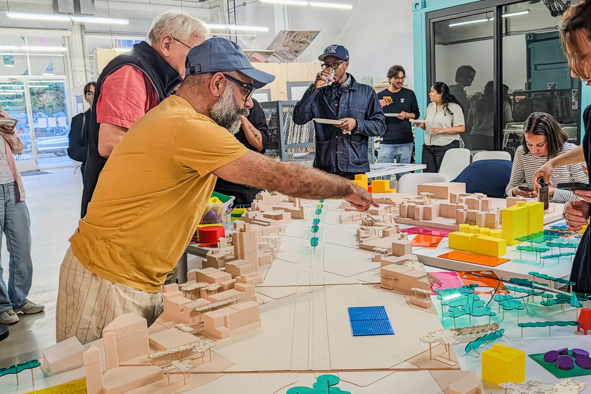 Interactive installation with wooden blocks and colorful translucent acrylic pieces arranged on a long table, participants building structures together.