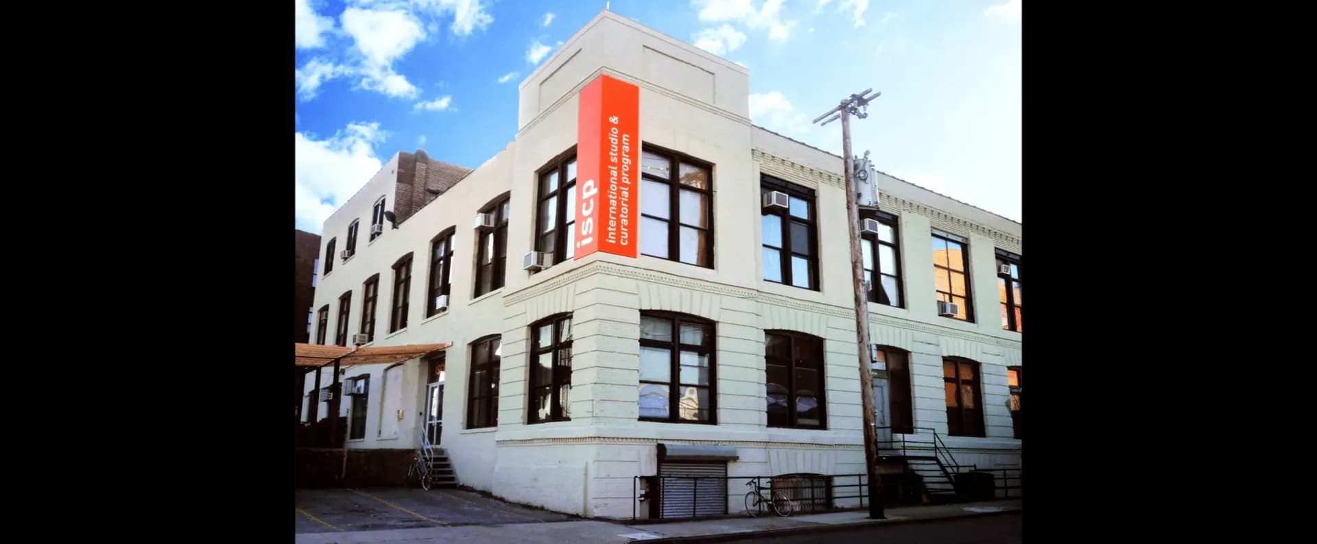 Exterior facade of the International Studio and Curatorial Program building with cream brick, dark-framed windows, and an orange sign reading ISCP