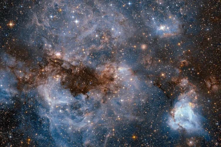 Astronomical photograph of nebula and star cluster with blue, white, and orange celestial bodies against dark space.