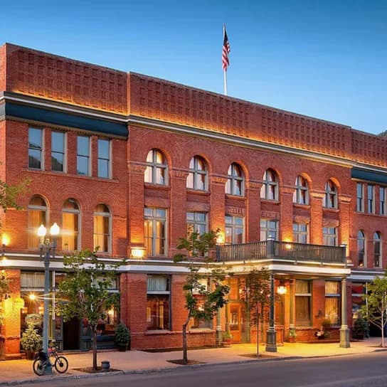 Exterior photograph of IRL Gallery's red brick storefront building at dusk, illuminated with warm lighting, featuring arched windows and an American flag.