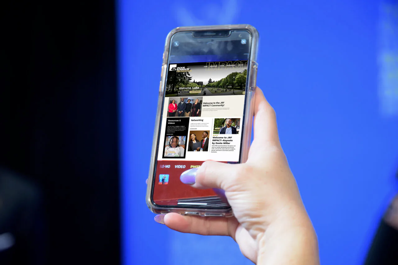 Hand holding smartphone displaying website homepage with landscape photo and article grid on blue background.