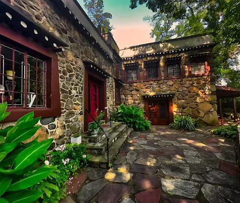 Stone and red-painted courtyard at Jacques Marchais Museum with arched doorways, lanterns, ivy, and tropical plants at sunset.