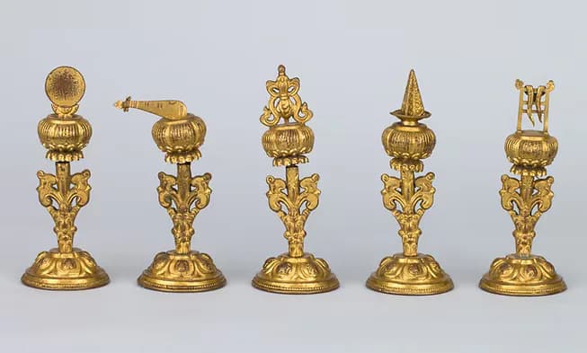 Five ornate gilt-bronze Tibetan Buddhist ritual objects with finials and decorative bases arranged in a row against neutral background.