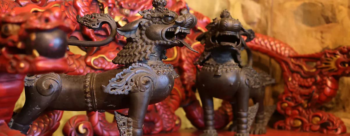 Dark bronze and black Tibetan animal sculptures displayed against vibrant red and gold patterned textile background.