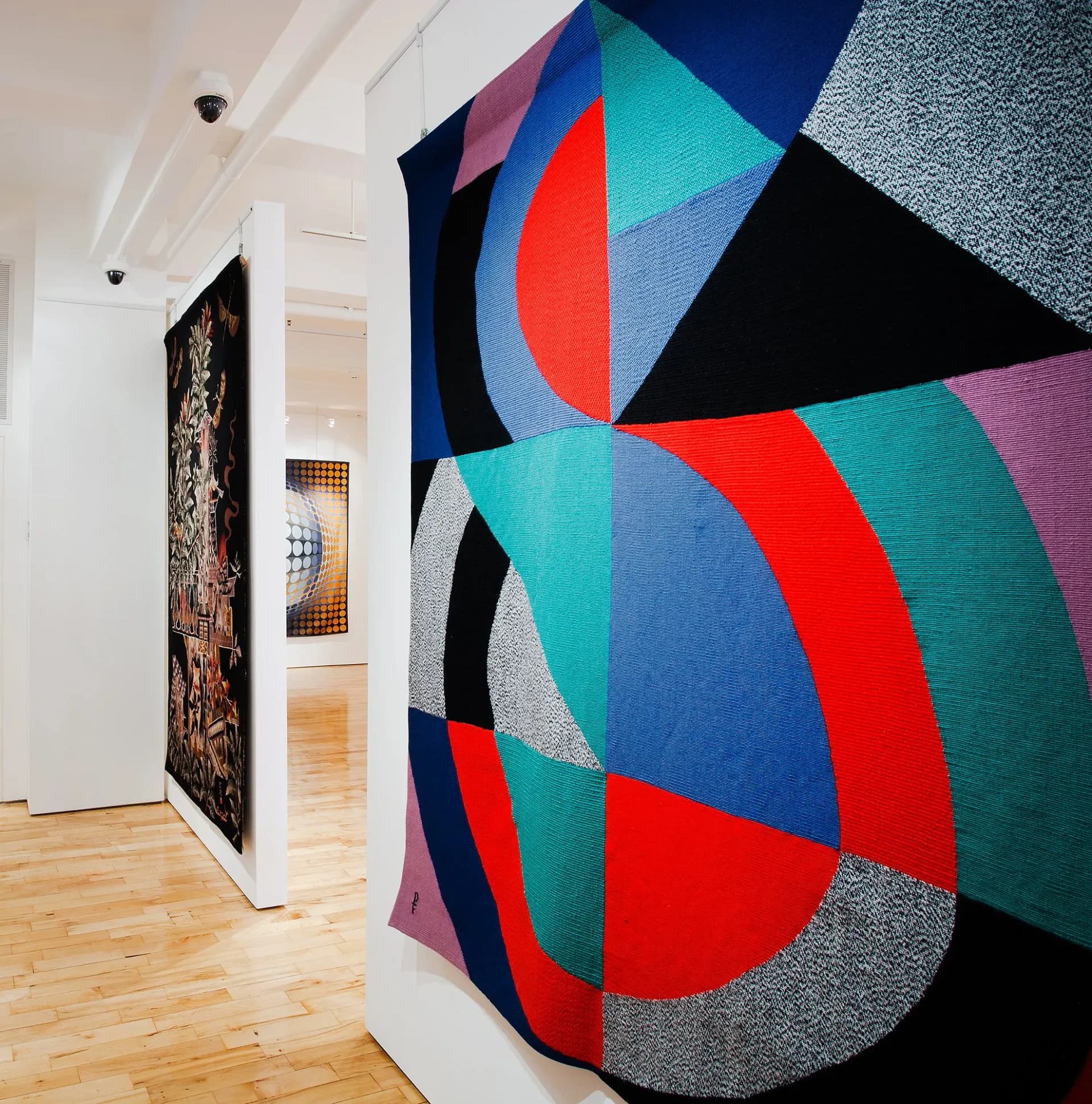 Interior of Jane Kahan Gallery showing a vibrant abstract textile wall hanging with geometric shapes in red, teal, blue, black, and gray tones.