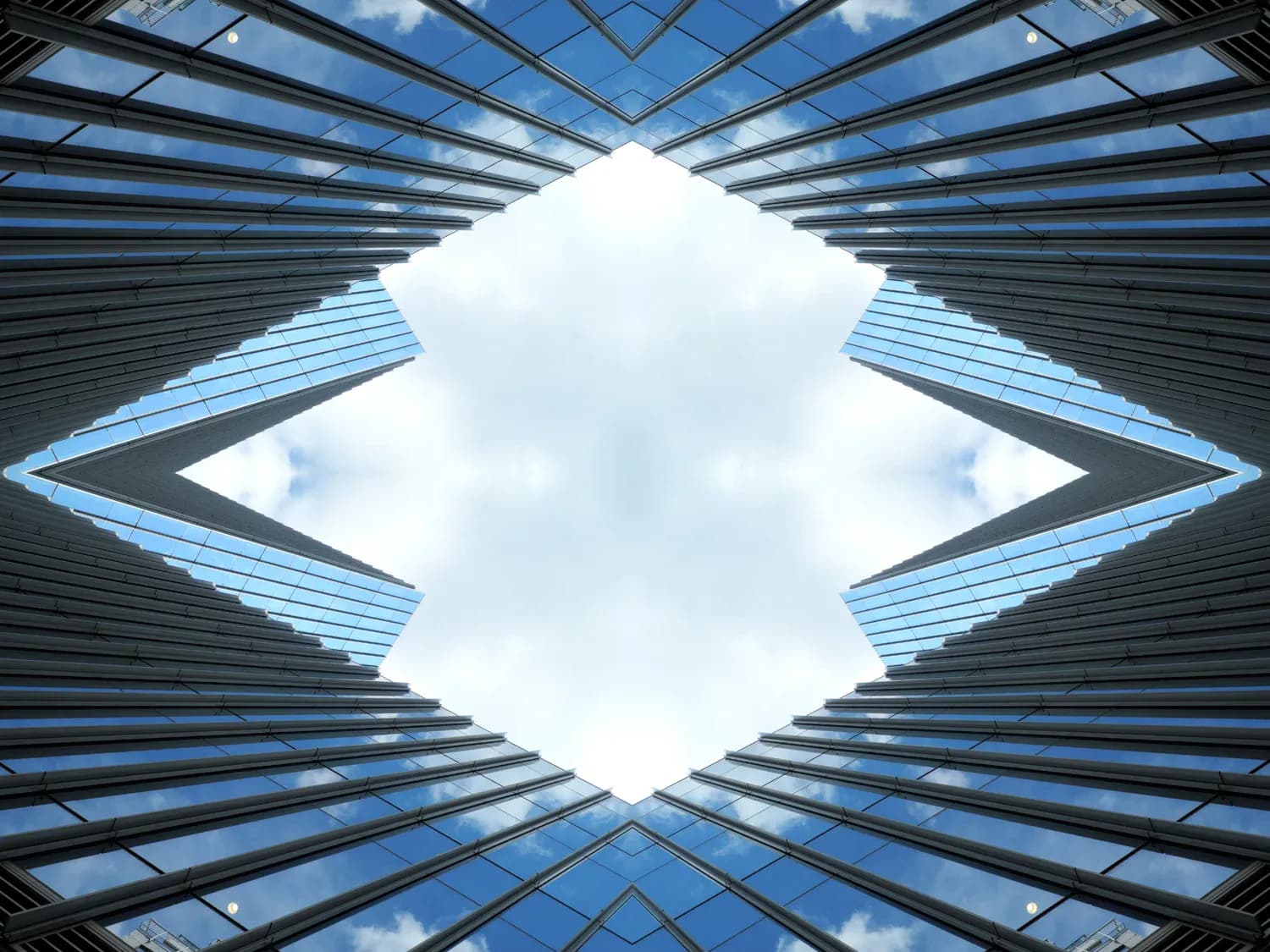 Symmetrical photograph of tall glass and steel buildings converging toward a diamond-shaped sky opening, shot from below with clouds visible.