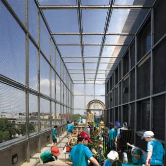 Rooftop play area of Jewish Children's Museum with glass ceiling, colorful playground equipment, and children in turquoise shirts supervised by adults.