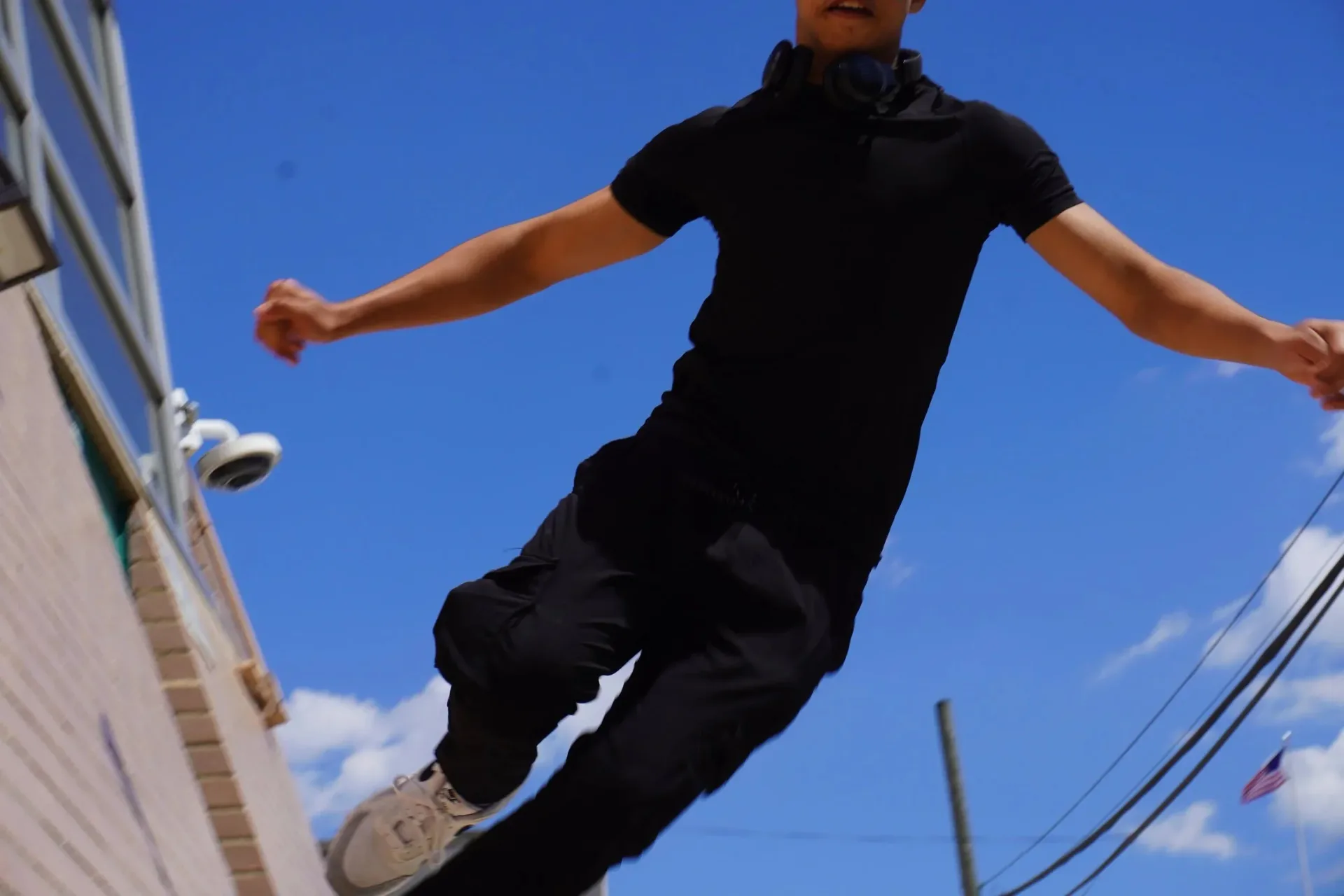 Person in black clothing mid-jump against blue sky, shot from below; dynamic action photograph.