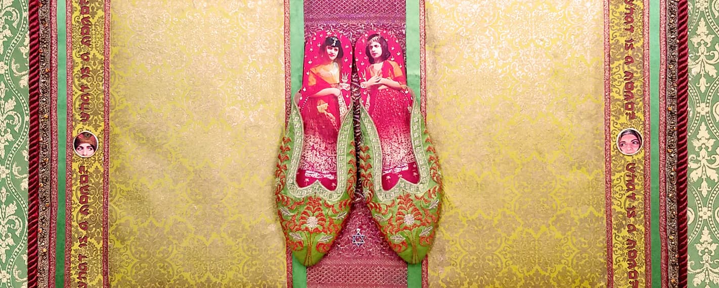 Ornate textile or fabric art featuring symmetrical pink and gold embroidered figures against pale yellow background with decorative borders.
