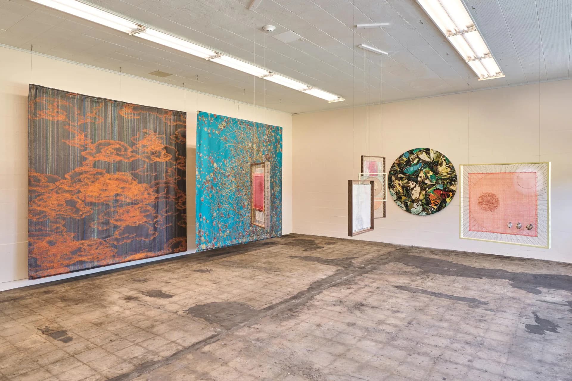 Kaufmann Repetto gallery interior with light wood flooring, white walls, fluorescent ceiling lights, and multiple abstract artworks including orange, blue, and mixed-media pieces.