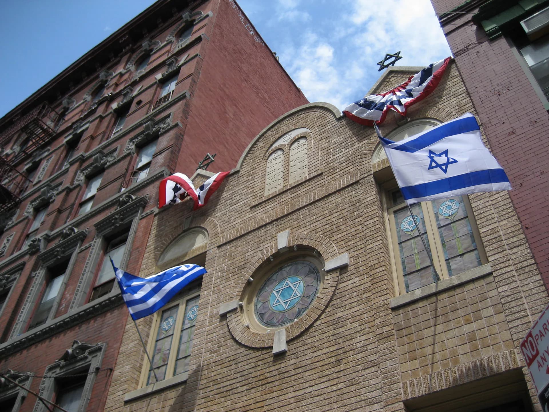 Exterior of Kehila Kedosha Janina Synagogue with stone façade, arched windows, Star of David window, and Israeli and Canadian flags displayed on the building.