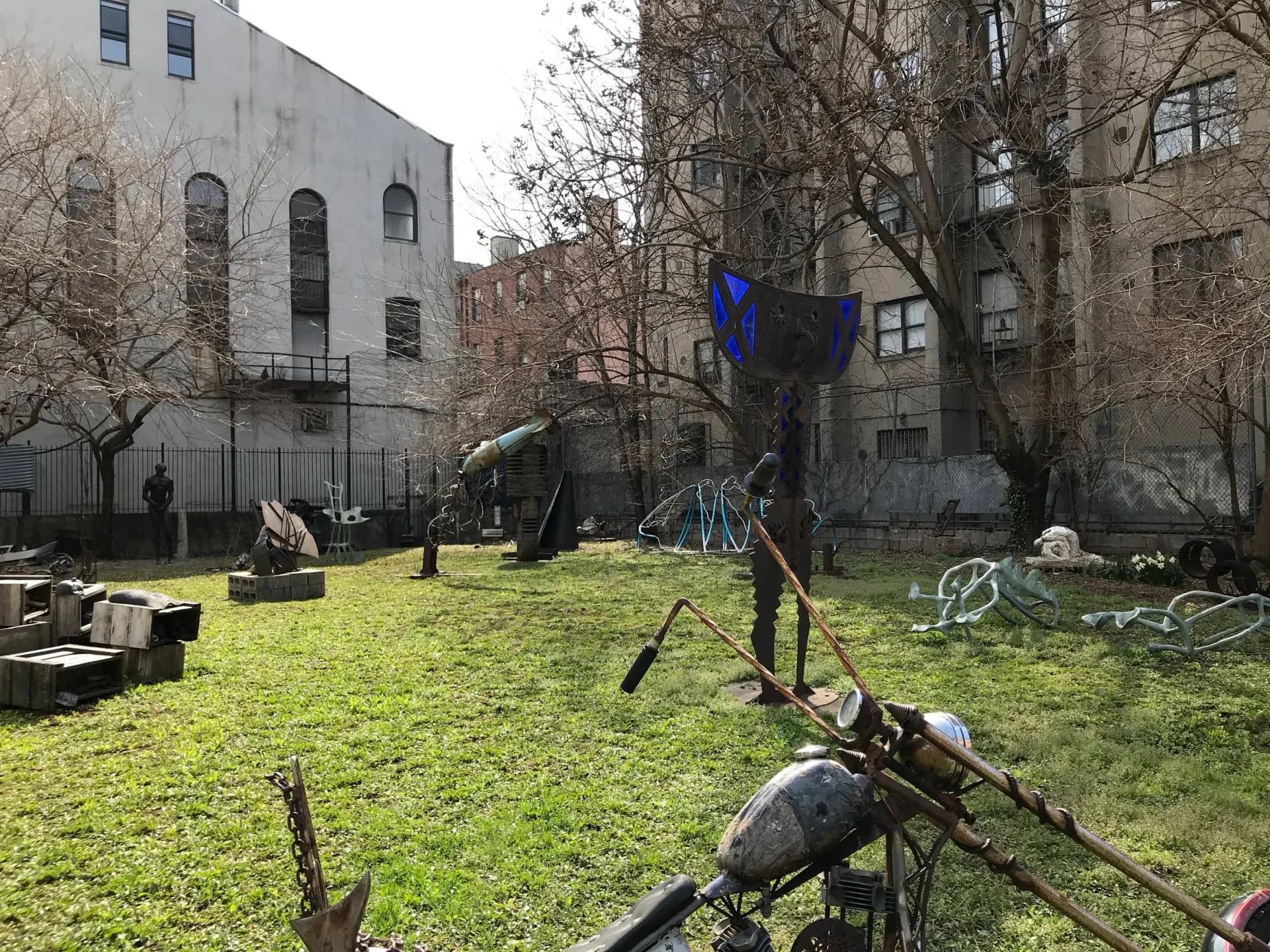 Outdoor courtyard at Kenkeleba House with metal sculptural installations on grass, bordered by brick buildings and bare trees.