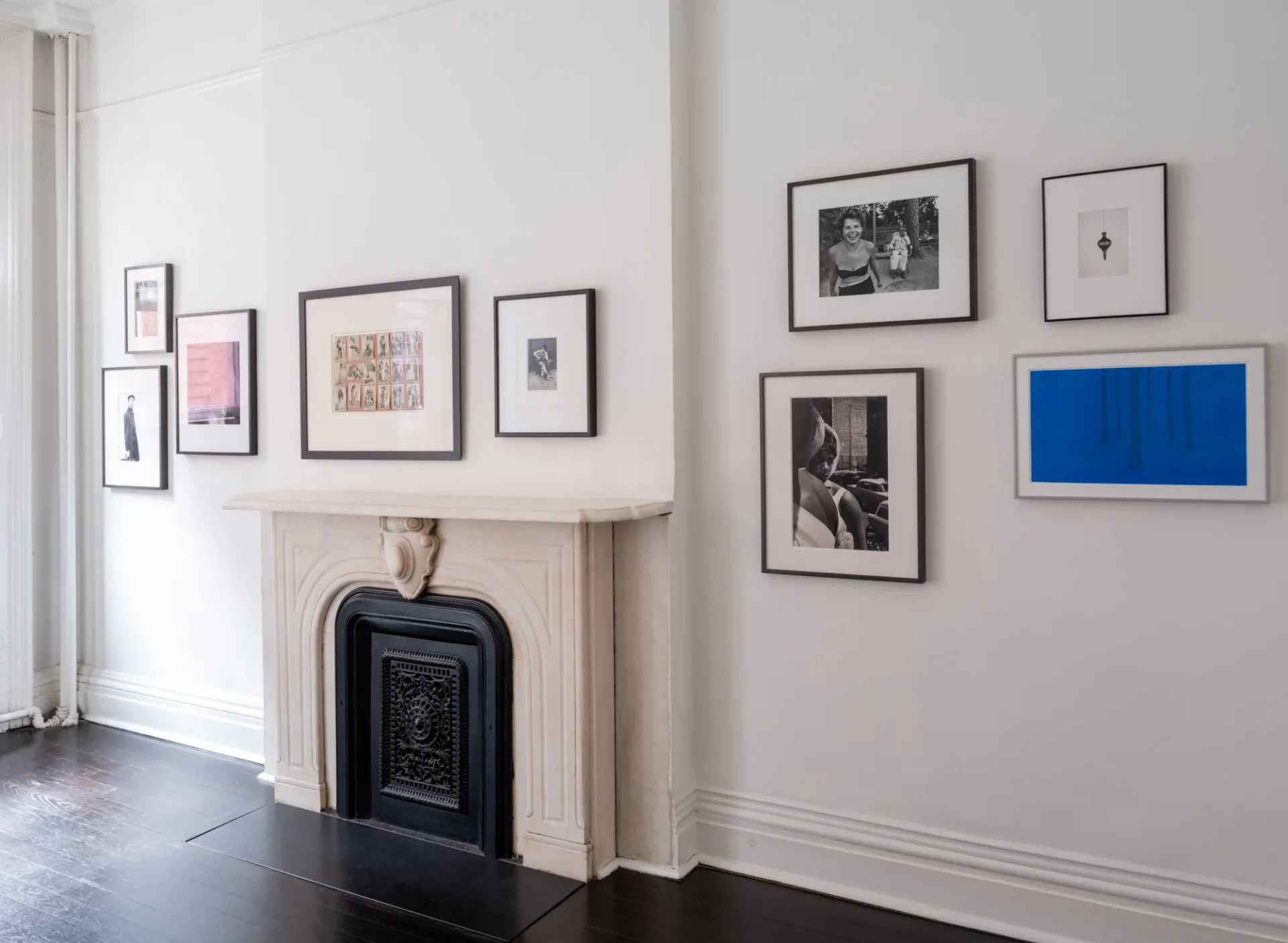 Gallery interior with white walls, dark wood floors, a marble fireplace, and framed photographs displayed on both walls