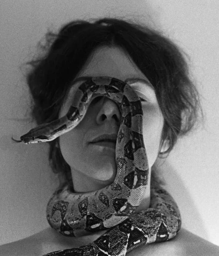 Black and white portrait of a person with a patterned snake draped across their face and neck.