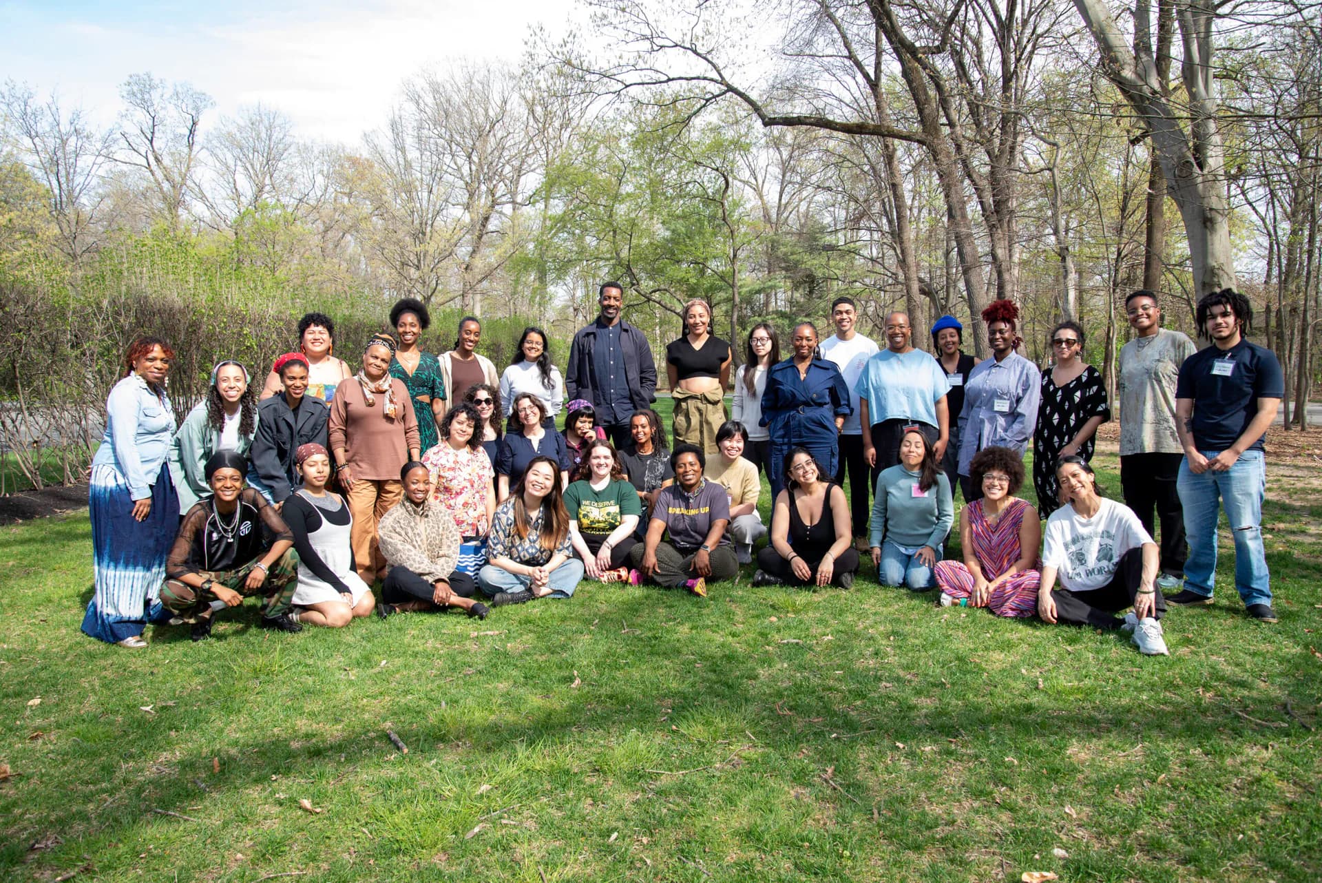 Group photograph of approximately 40 people posing together outdoors on a grassy area with bare trees, likely at a Laundromat Project community gathering or event.