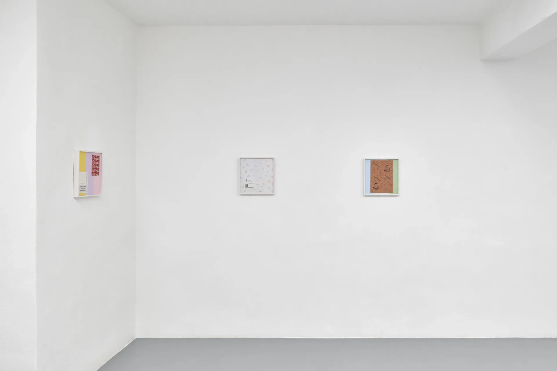 Clean gallery wall with three small artworks spaced horizontally: colorful abstract piece on left, white center work, and brown textured piece on right.