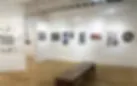Gallery interior at LIC Artists with white walls hung with small artworks, wooden floor and a bench