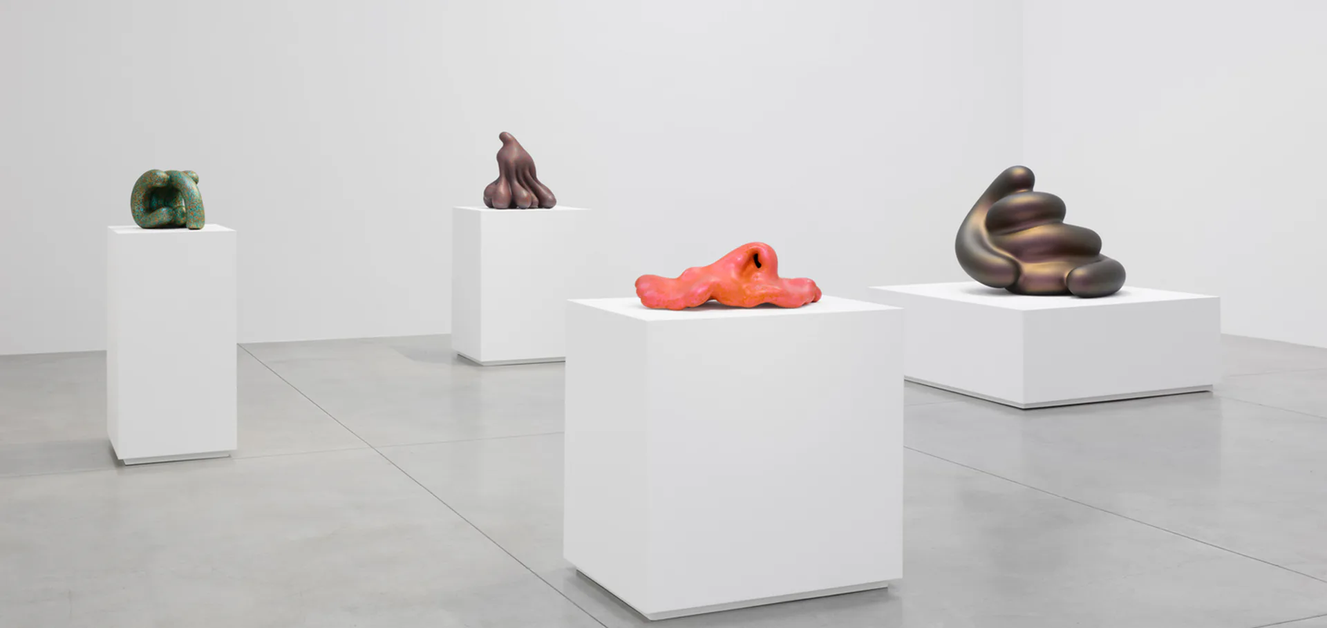 Lisson Gallery interior with white pedestals displaying sculptural artworks in varied materials and colors including green, brown, red, and dark forms on polished floor.