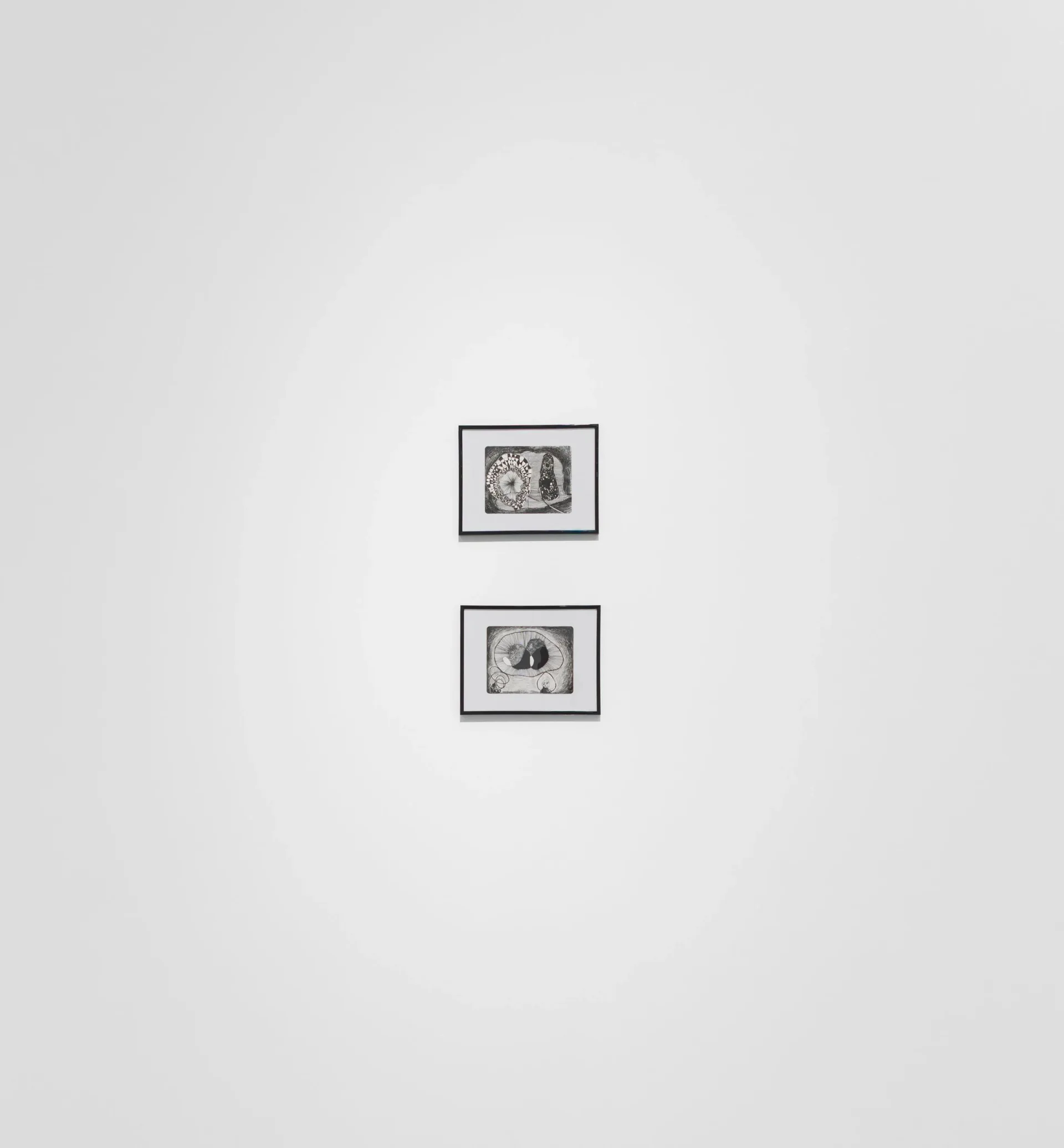 Two black-framed small artworks vertically stacked on white gallery wall with significant spacing.