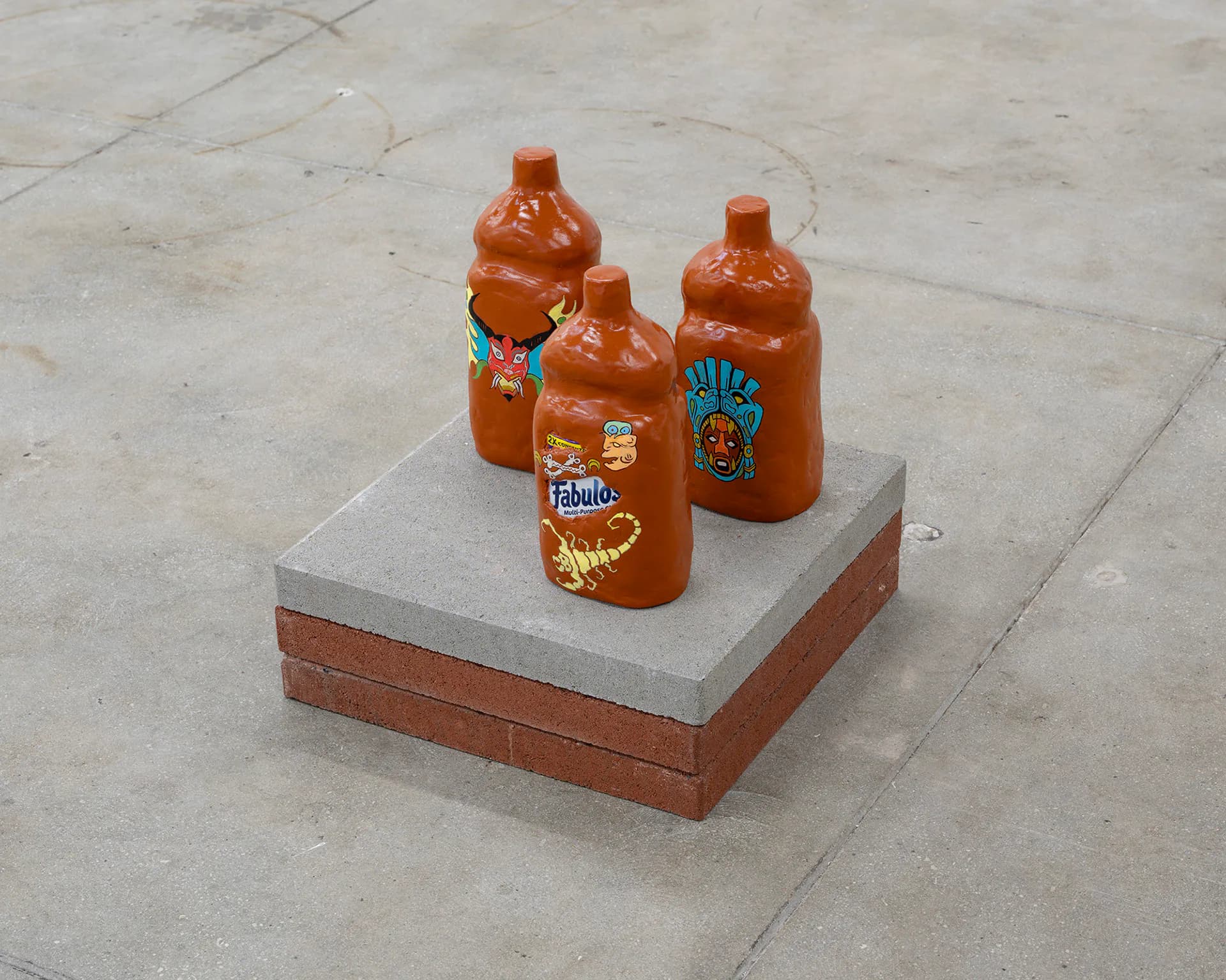 Three orange ceramic vessels with decorative patterns and text arranged on a concrete and brick platform in an industrial setting.