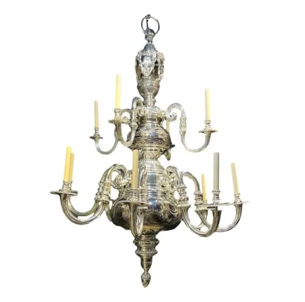 Two-tiered brass chandelier with ornate finial and multiple curved arms supporting candle holders, classical European design.