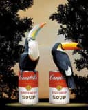 Mixed-media pop art depicting two stylized figures pouring soup from oversized Campbell's soup cans against a dark foliage background.