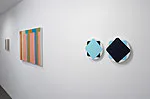 Interior gallery view showing three framed artworks mounted on a white wall—books on left, and geometric shapes on right.