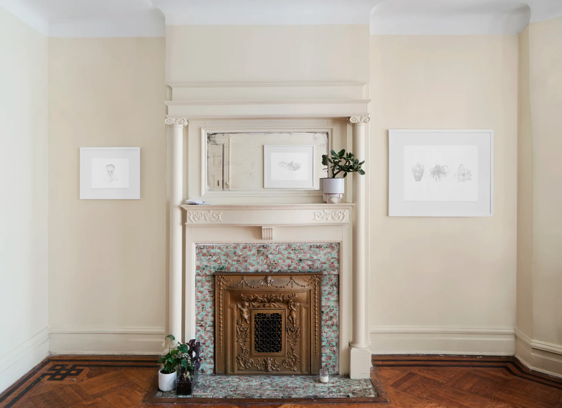 Interior corner of Medium Tings with a decorative fireplace and framed artworks hung on cream walls above a parquet wood floor