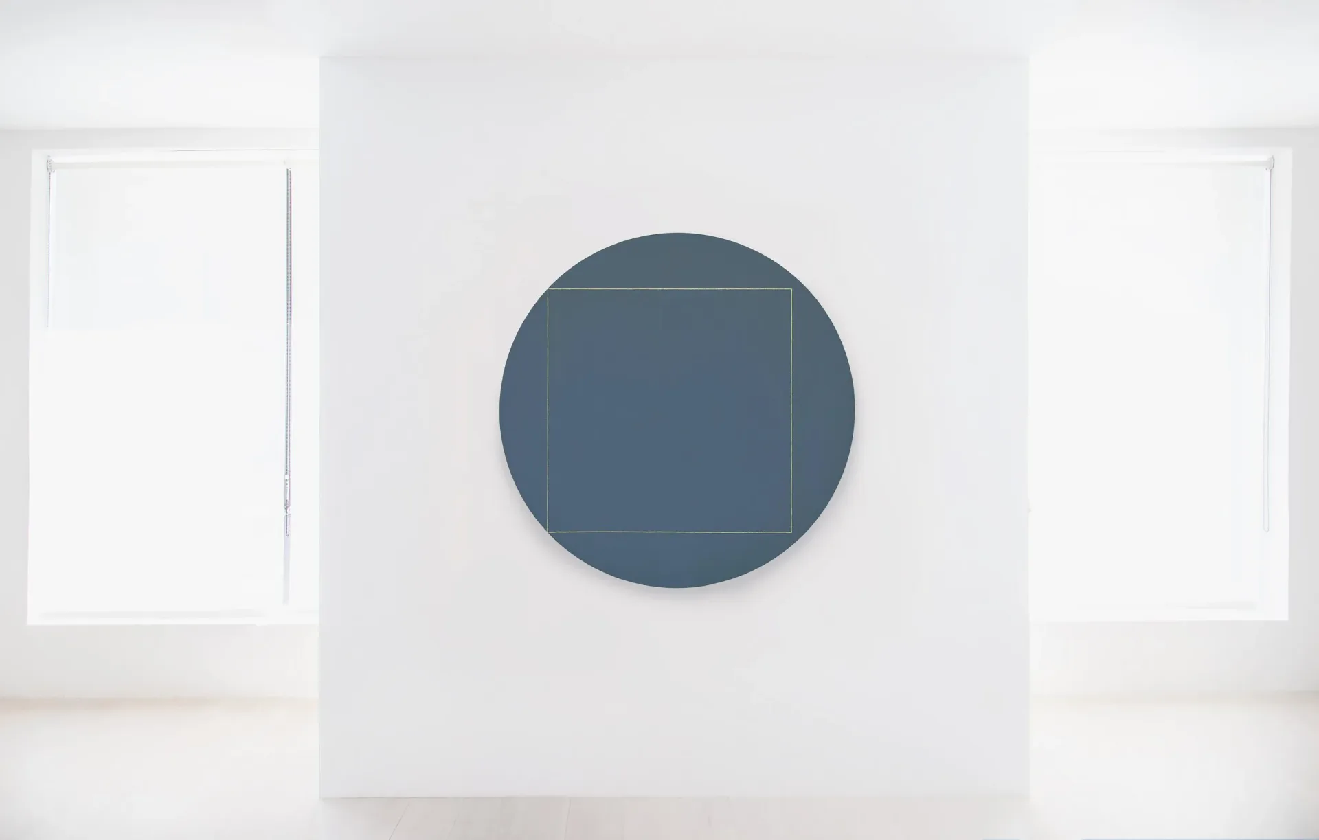 Minimalist gallery interior with white walls and floor, centered dark blue circular sculpture with internal square, flanked by white doorways.