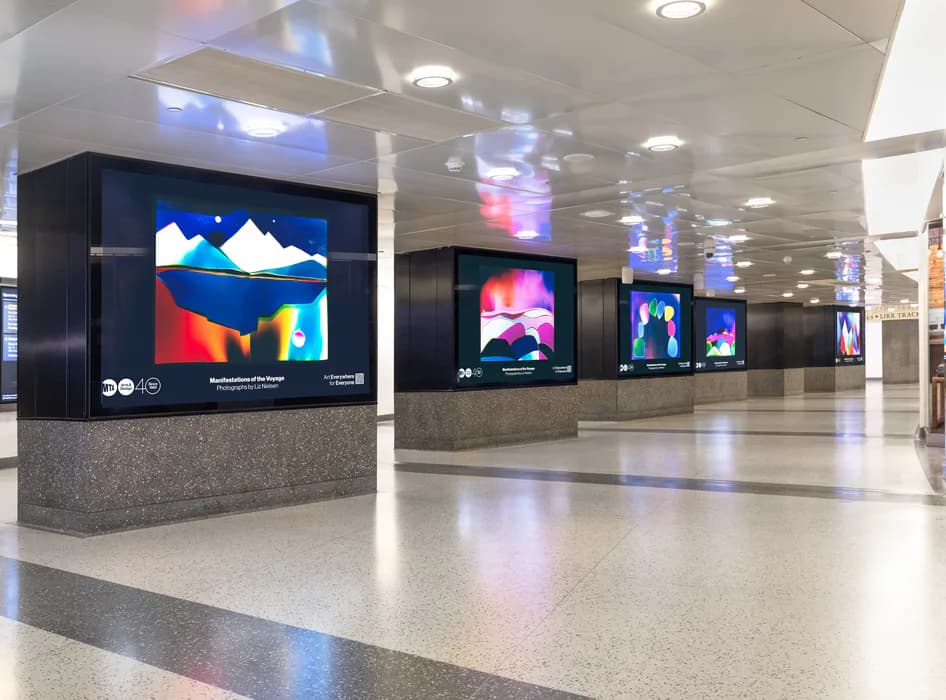 Modern gallery interior with polished concrete floor and recessed ceiling lights, displaying multiple large digital screens mounted on black kiosks showing colorful abstract imagery.