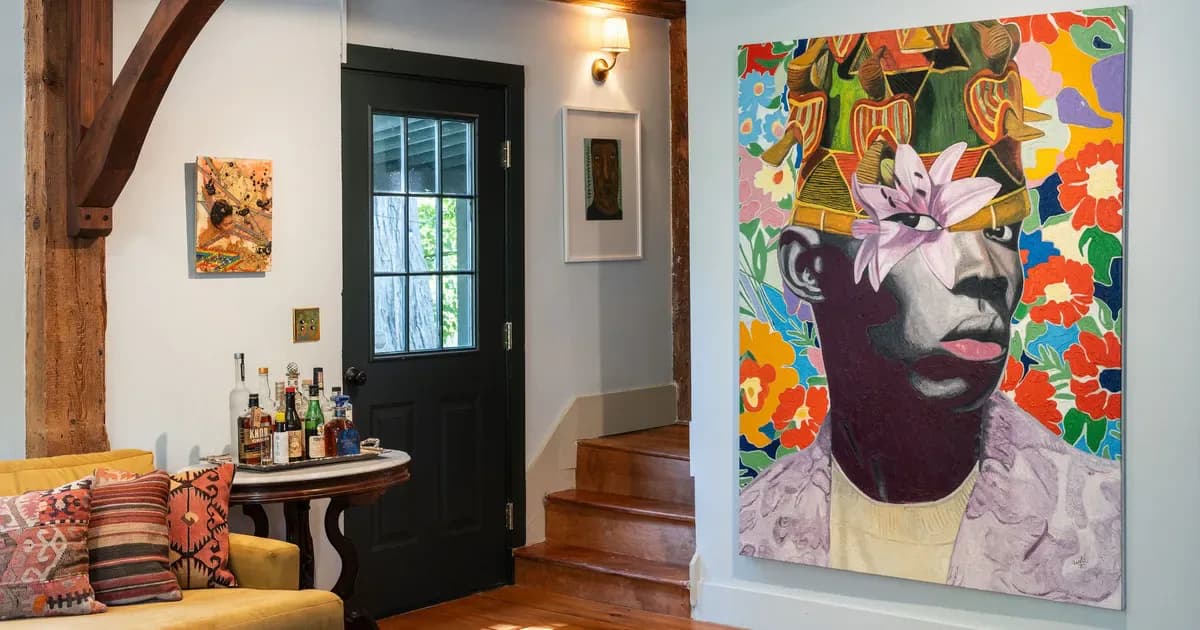 Interior of MONTAGUE CONTEMPORARY gallery showing white walls, wooden beams, black door, staircase, colorful abstract portrait artwork on right wall, and decorative pillows on seating area.