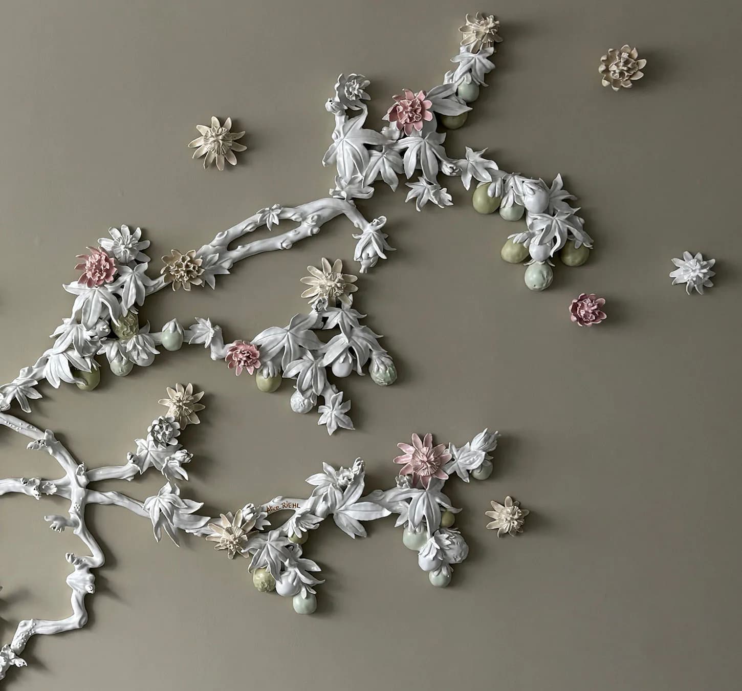 White sculptural relief with ornamental floral branch design featuring delicate flowers and leaves with pink and cream accents on neutral background.