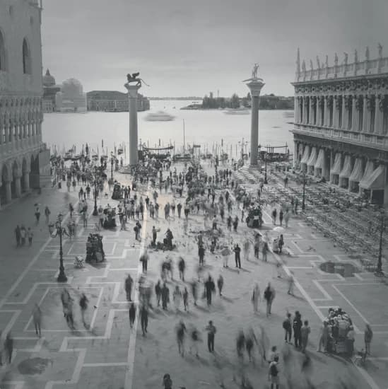 Black and white overhead photograph of Venice's St. Mark's Square with scattered pedestrians, ornate Venetian architecture and water visible.