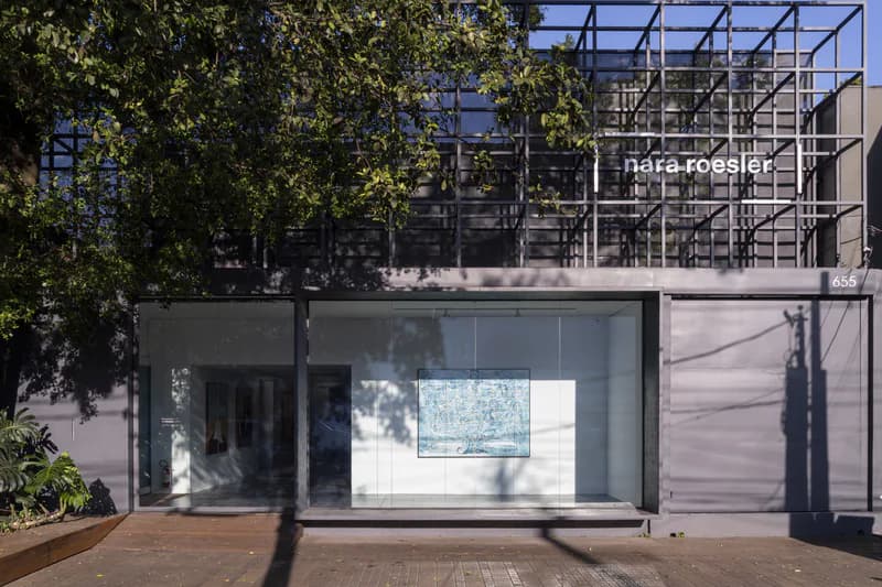 Exterior facade of Nara Roesler gallery with a metal grid canopy, large glass storefront window, and trees in front