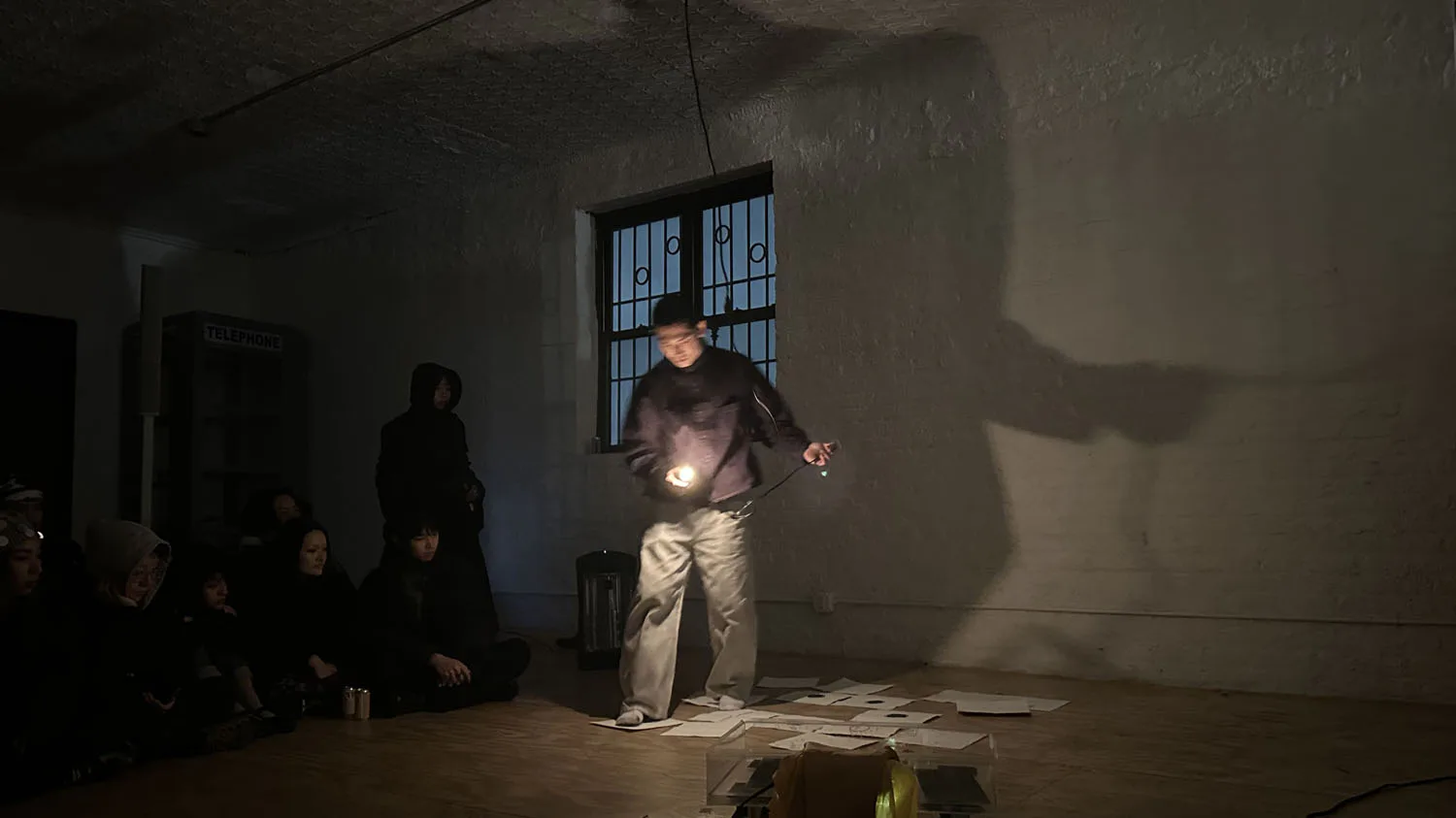 Person standing in darkened gallery space holding illuminated spherical object; performance or installation artwork with dramatic lighting.