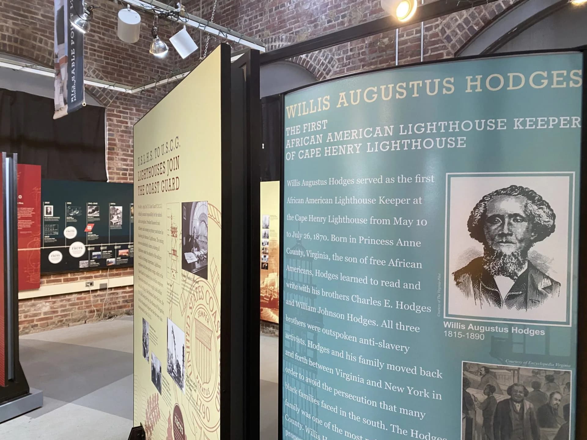 National Lighthouse Museum gallery interior with brick walls displaying exhibition panels about Willis Augustus Hodges, the first African American lighthouse keeper, including portrait and historical information.