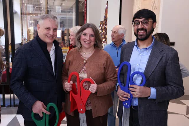 Four adults pose indoors holding colorful mathematical shapes in red and blue; gallery interior with windows visible behind.