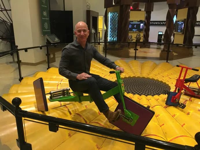 Man crouches on large yellow interactive mathematical installation with colorful geometric objects at National Museum of Mathematics.