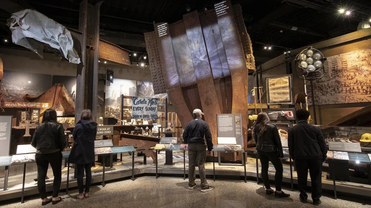 Museum gallery showing large steel beam structure, artifacts, and visitors in exhibition space.