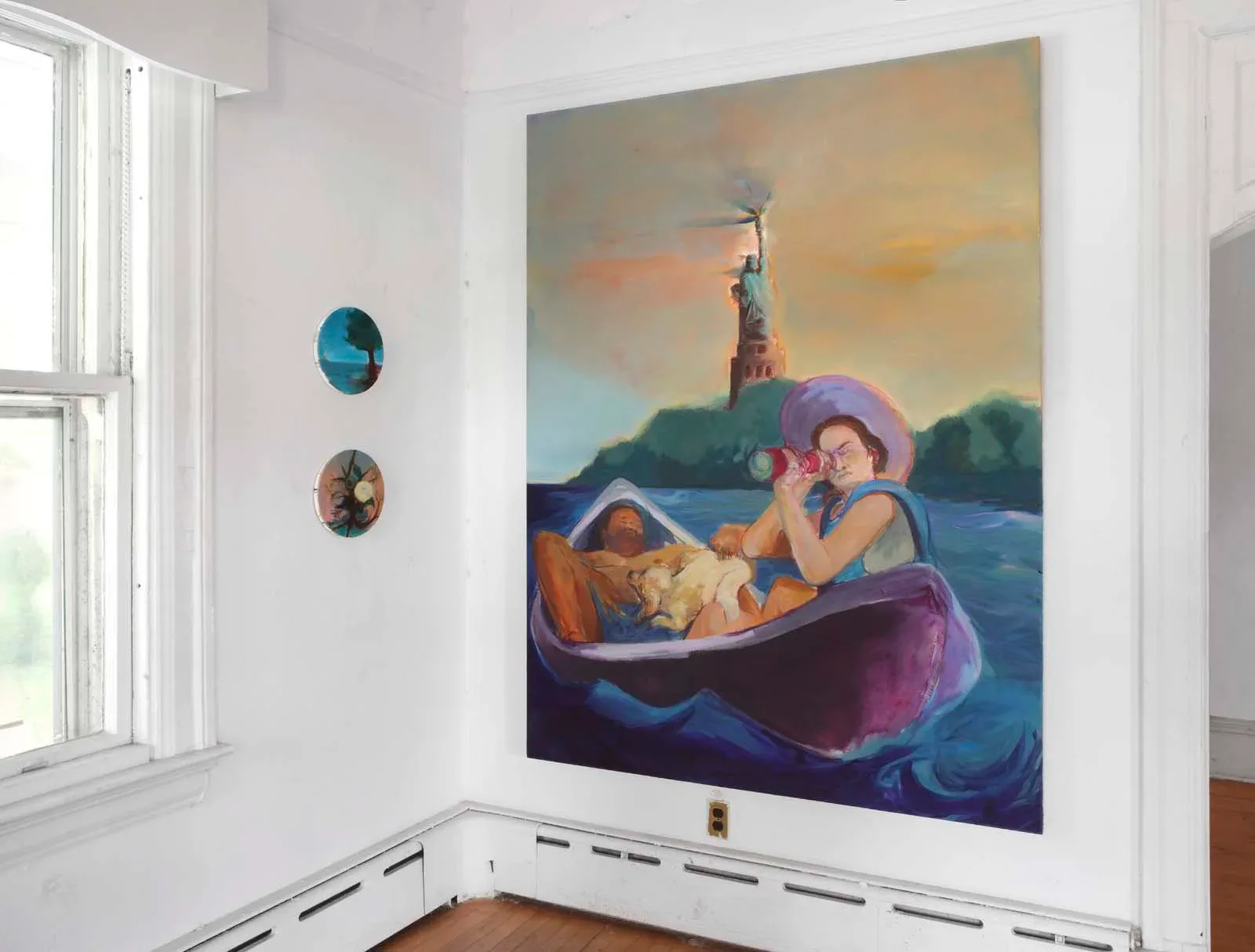 Gallery interior with white walls and wooden floor, large colorful painting mounted on wall depicting figures in a boat with statue-like structure, small circular artworks on adjacent wall.
