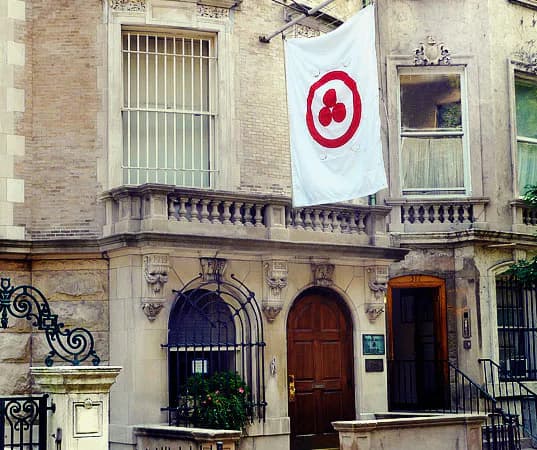 Exterior facade of the Nicholas Roerich Museum townhouse with arched wooden door, iron gates, and a red-and-white banner hanging above the entrance