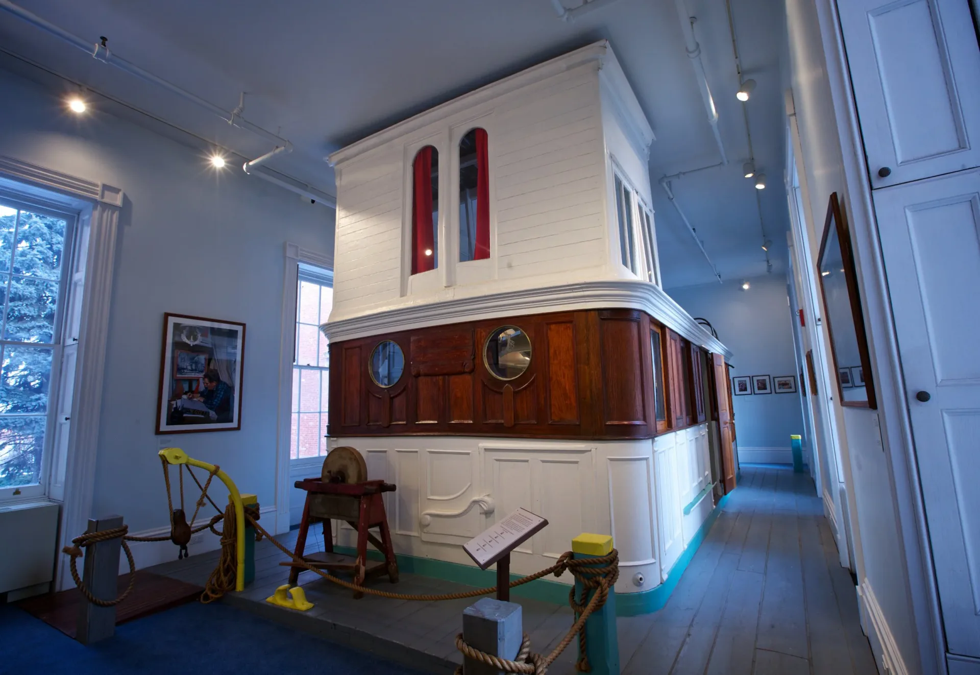 Noble Maritime Collection gallery interior: white and wood-toned miniature ship model installation on platform, nautical artifacts, recessed lighting, wooden floors.