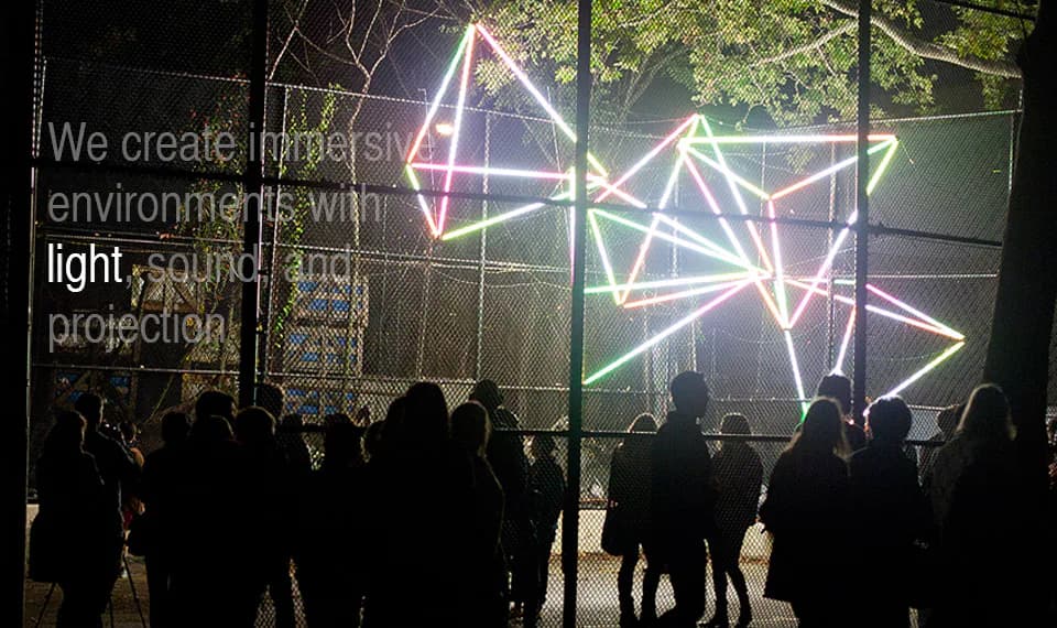 Crowd silhouetted against a glowing geometric light sculpture strung with neon-colored lines at night during a Nuit Blanche New York installation.