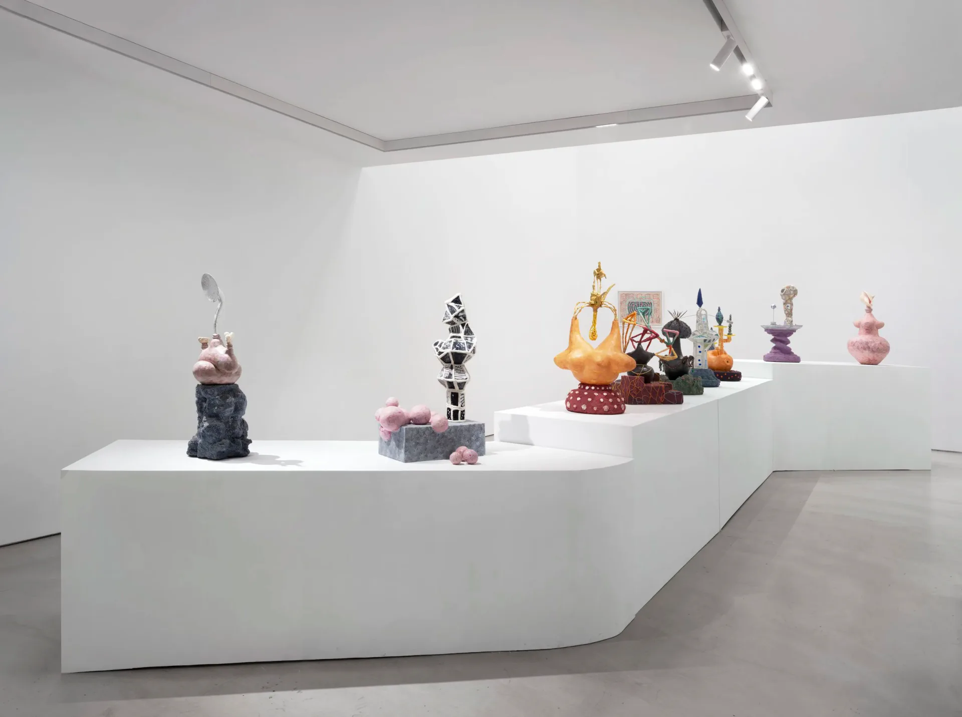 Gallery interior at Nunu Fine Art with white curved display counter holding colorful sculptural objects and decorative pieces under track lighting.