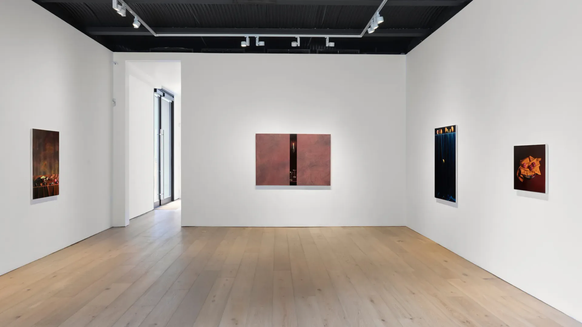 Modern gallery interior with wooden floor, white walls, black ceiling grid, and five artworks displayed: hanging vertical piece and four framed paintings in varied colors including burgundy and black.