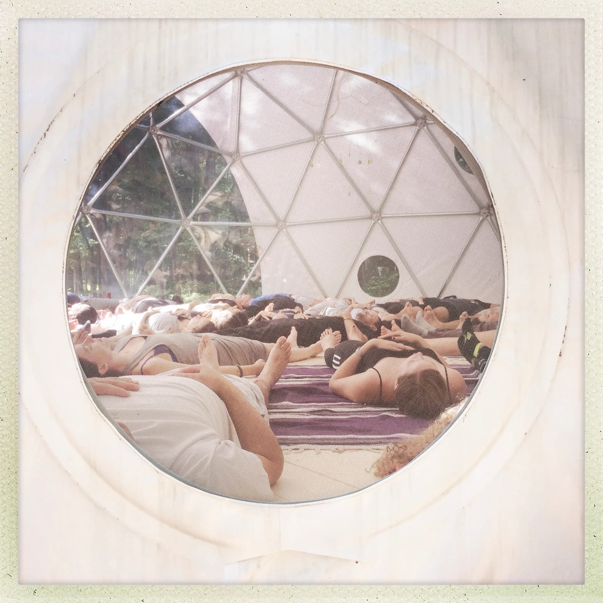 Polaroid-style photograph showing people lying on platforms inside a geodesic dome structure with triangular framework and natural light.