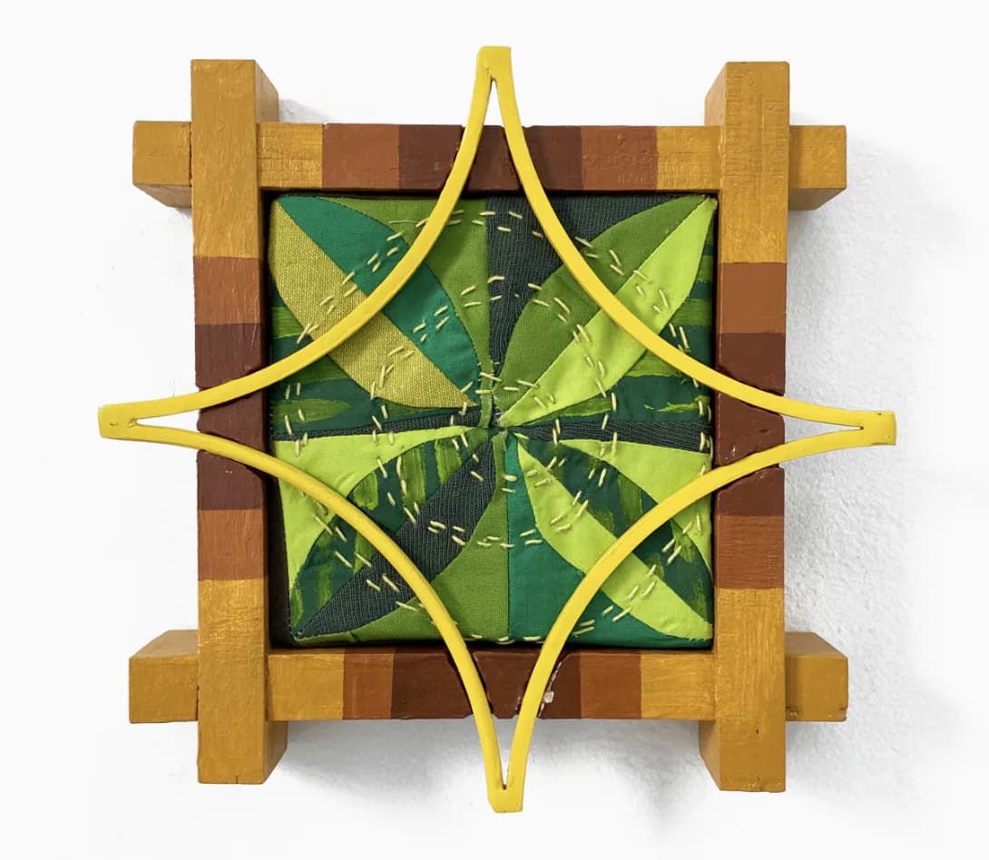 Mixed-media installation combining wooden geometric frame, green plant photograph, and bright yellow ribbon forming a star pattern.
