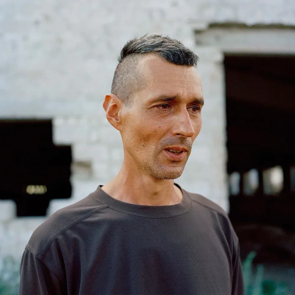 Portrait of a man in black t-shirt against white building exterior, looking to the side.