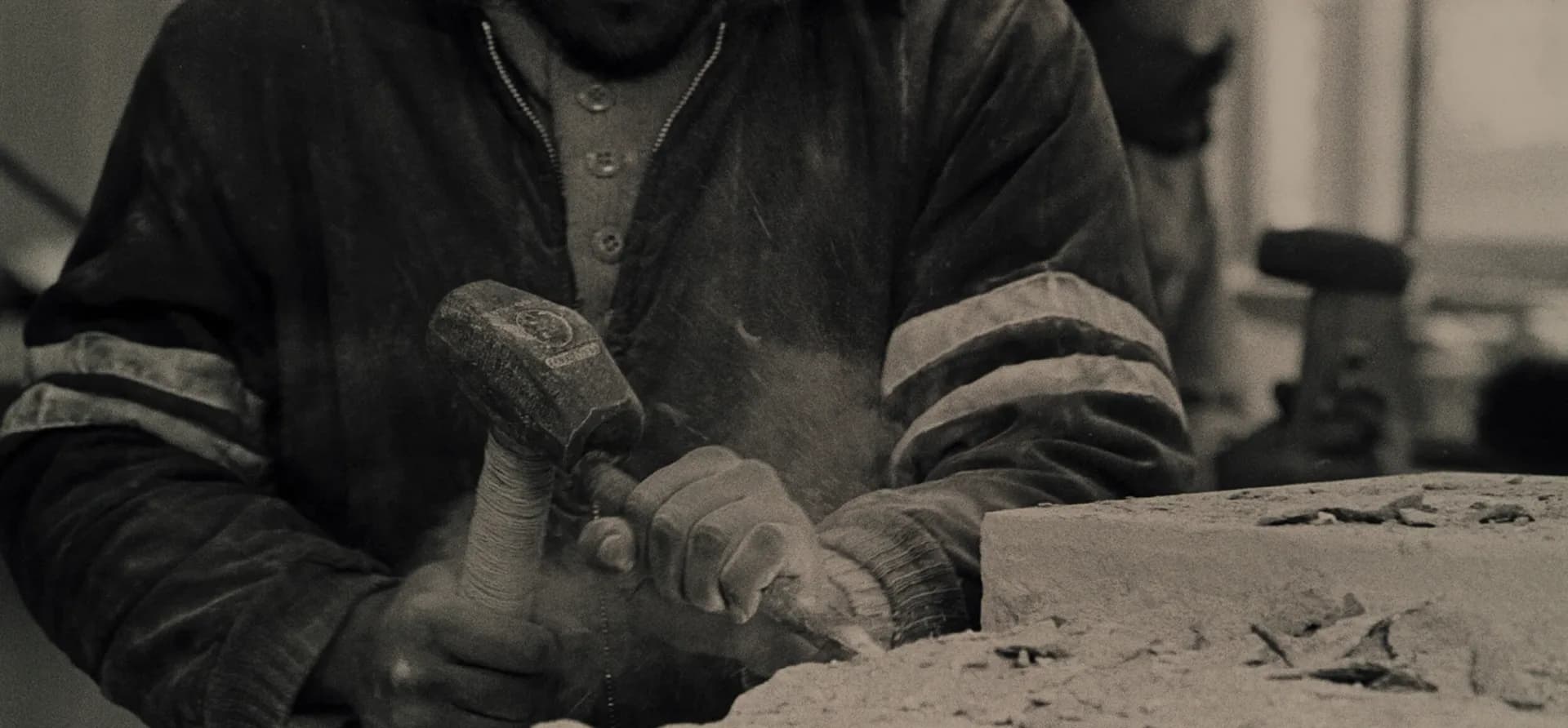 Close-up black and white photo of hands using a hammer and chisel to carve stone at Pellettieri Stone Carvers' Academy